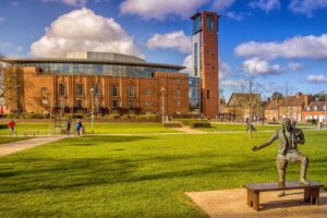 North fascade of the Royal Shakespeare theatre. A large brick building with a tower. A statue in the foreground.