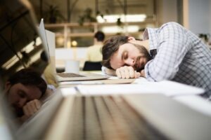 A young adult man with brown hair is slumped on a laptop desk asleep