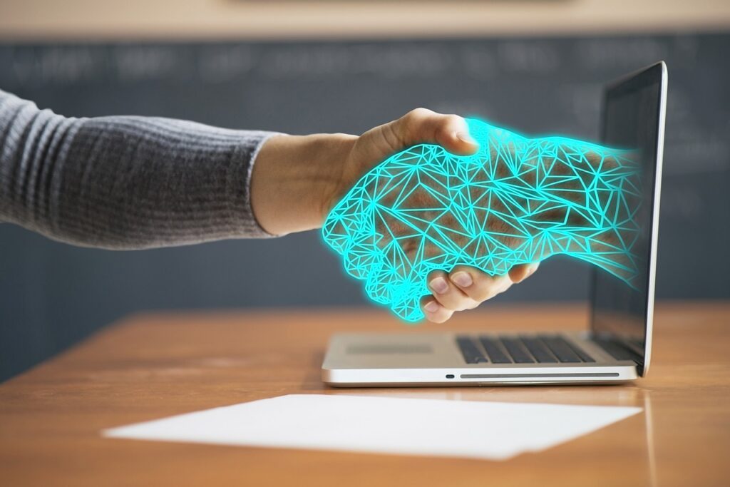 Human hand shaking a hand made of energy coming out of a laptop screen.