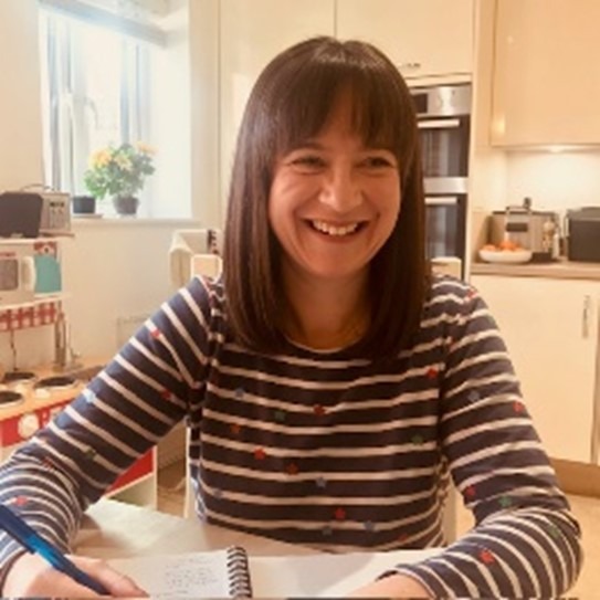 Tamsin is a white woman with dark shoulder length hair and is wearing a blue and white striped t-shirt.