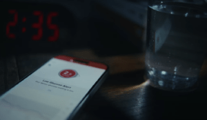 A mobile phone on a bedside table flashing 'low glucose alert'.