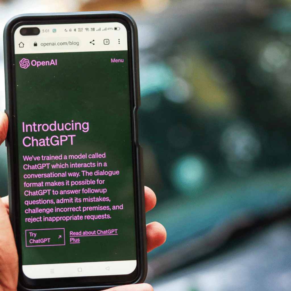 A person holding a smartphone displaying the OpenAI website introducing ChatGPT, with text about its conversational AI features.